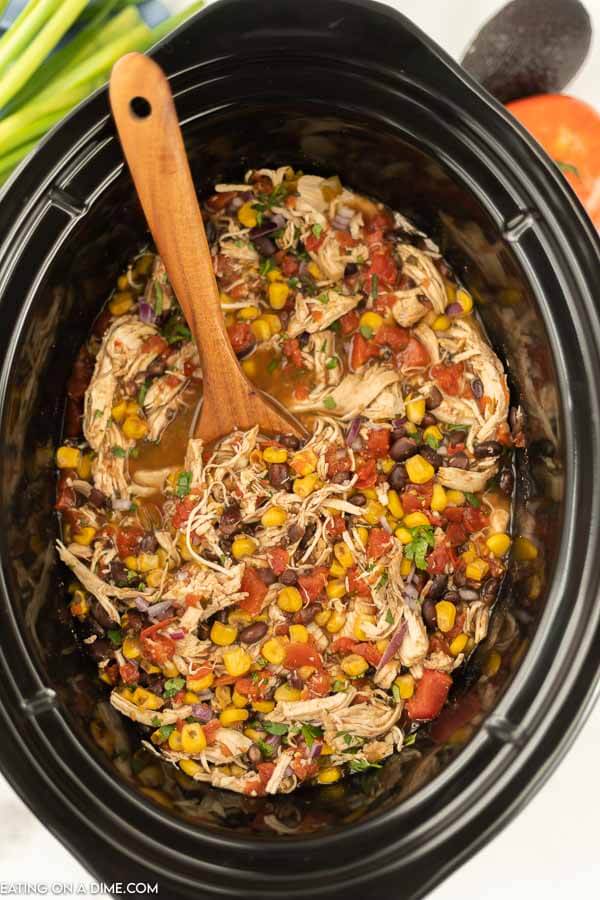 Close up image of santa fe chicken in the crock pot with a wooden spoon. 