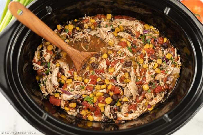 Close up image of santa fe chicken in the crock pot with a wooden spoon. 