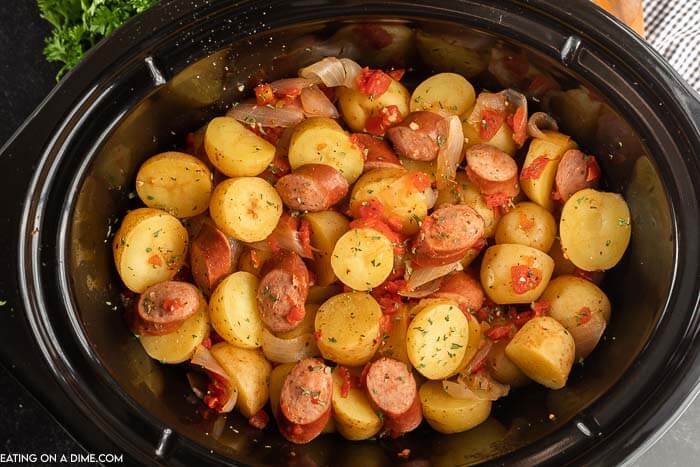 Overview of crock Pot Sausage and Potatoes in a black crock pot topped with fresh parsley.  