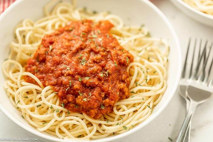 Close up image of a plate of spaghetti noodles with spaghetti sauce on top with two forks on the side, 