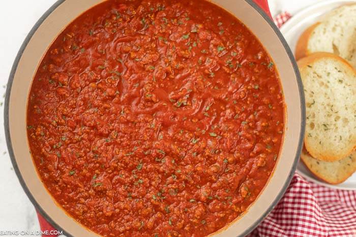 Close up image of spaghetti sauce being cooked in a dutch oven with a side of french bread. 