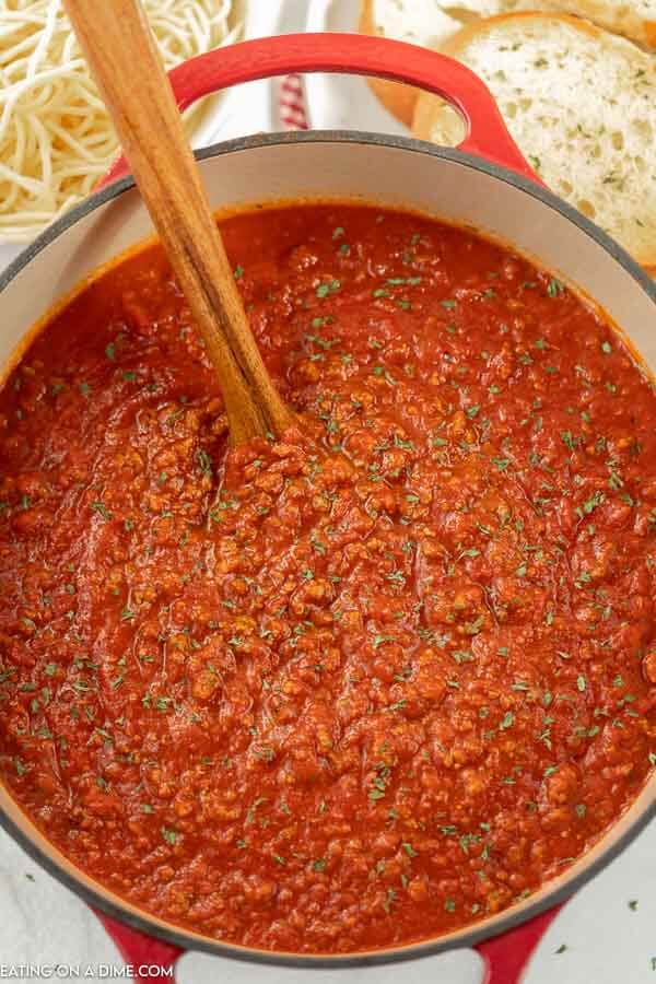 Close up image of spaghetti sauce in a dutch oven with a wooden spoon. 