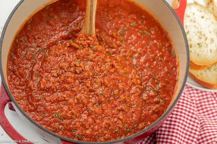 Close up image of spaghetti sauce in a dutch oven with a wooden spoon mixing it. 