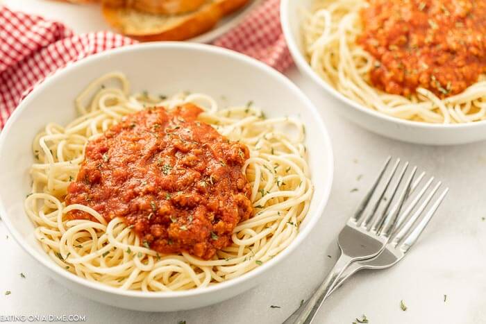 Close up image of two white bowls of spaghetti and meat sauce on top with two forks. 