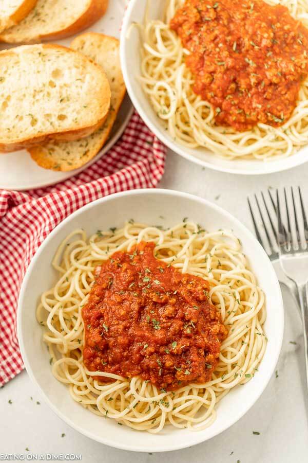 Close up image of two white bowls of spaghetti with sauce with a side of bread. 