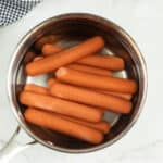 Hot dogs in a pot on a marble counter.