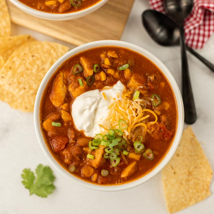 A bowl of tex mex chicken chili topped with sour cream, shredded cheese and diced green onions 