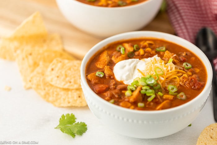 A white bowl of chili topped with cheese, sour cream, and green onions