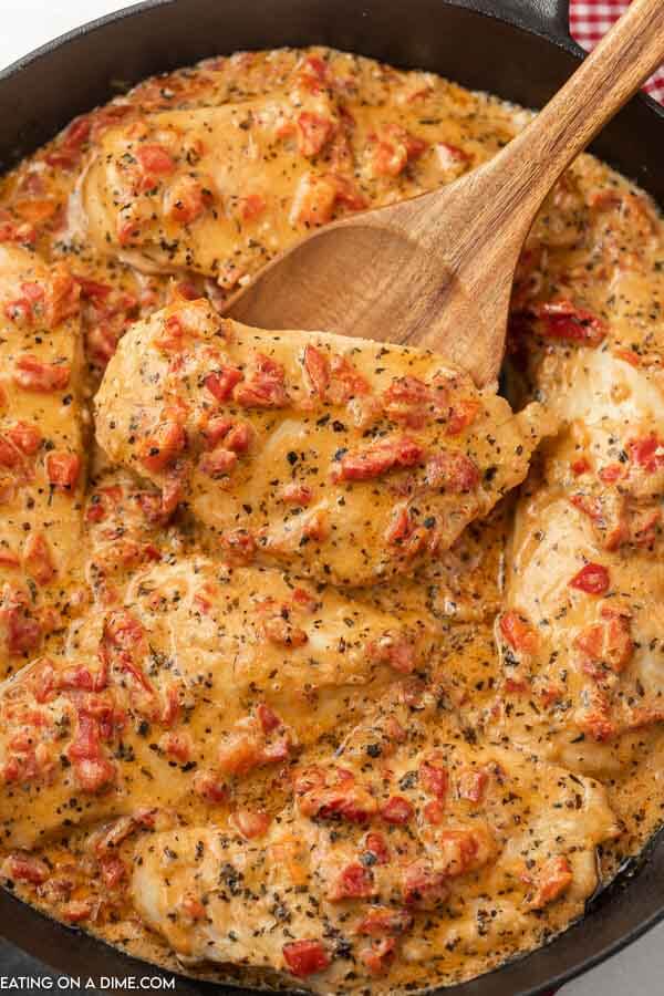 Close up image of roasted red pepper chicken in a skillet and a serving on a wooden spoon 