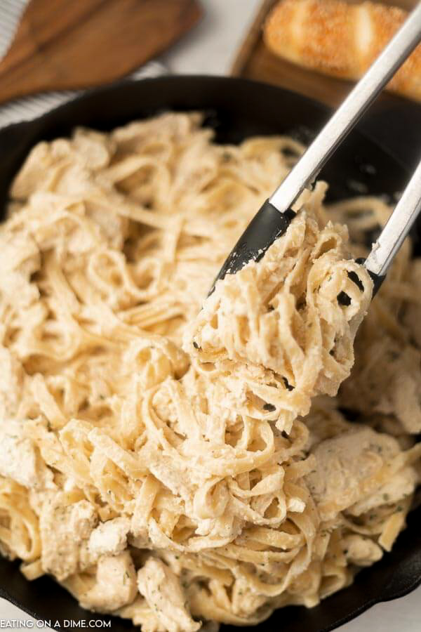 Close up image skillet chicken alfredo with a serving on tongs. 