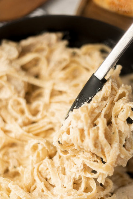 Close up image skillet chicken alfredo with a serving on tongs. 