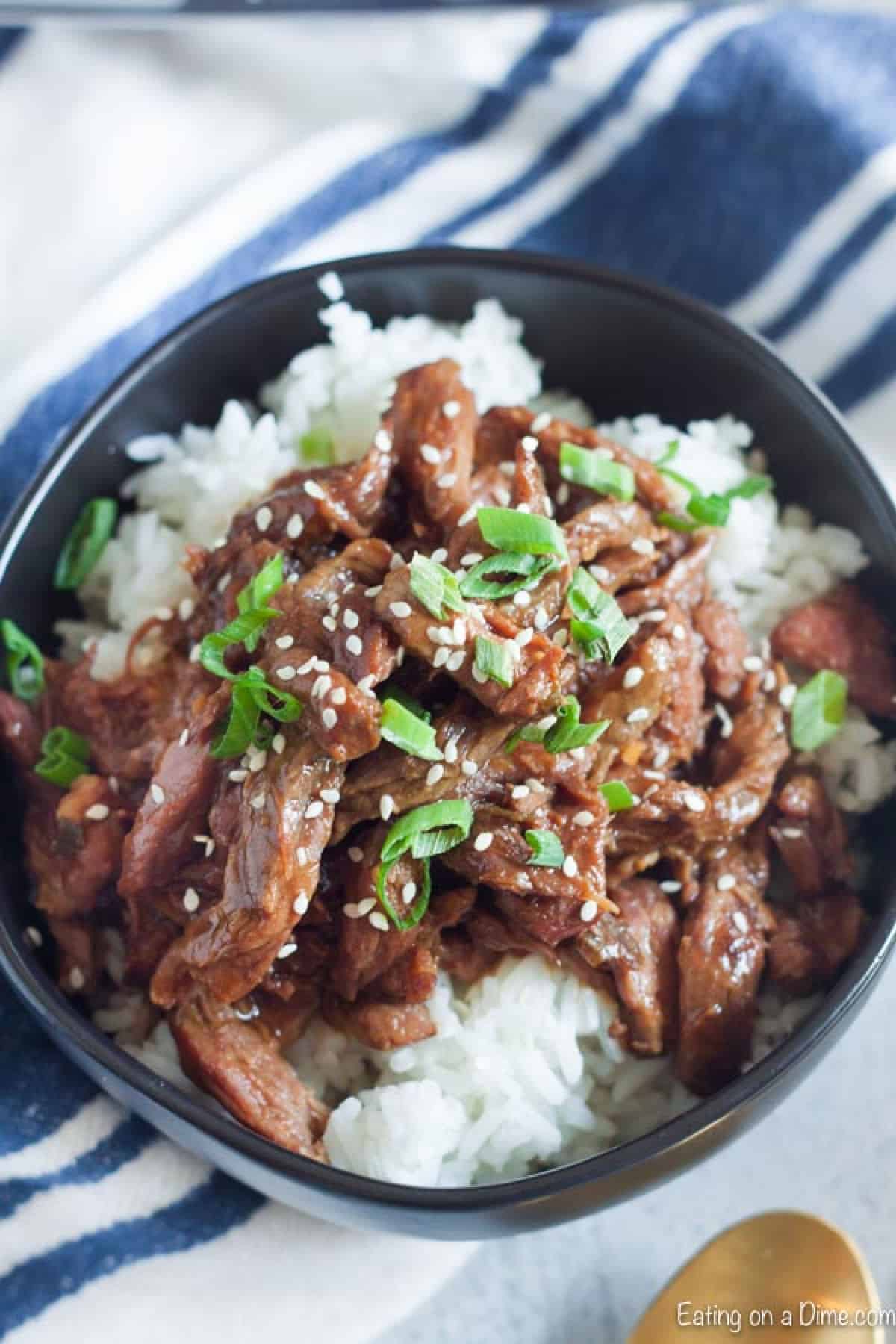 Close up image of sesame beef on rice in a black bowl.