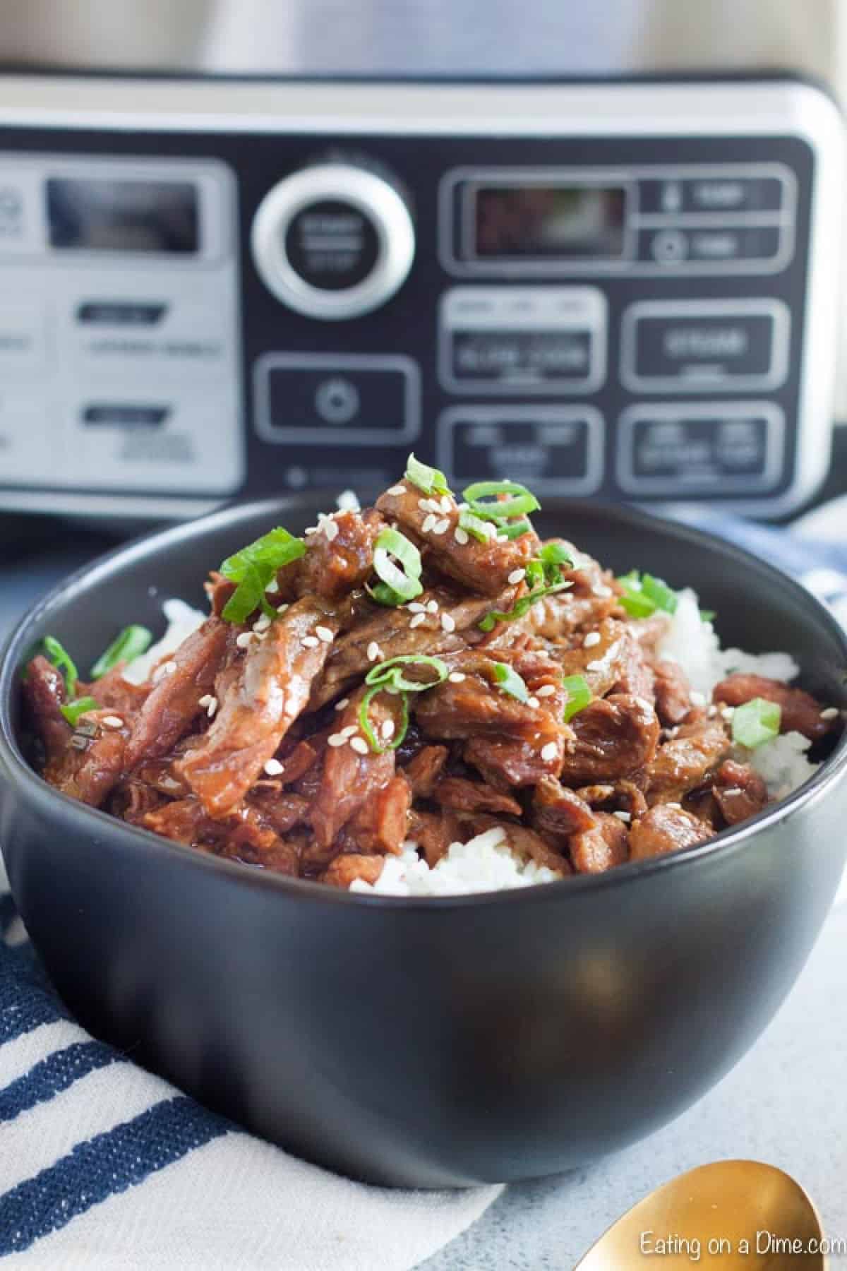 Close up image of sesame beef on rice in a black bowl.