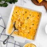 A square white baking dish filled with creamy, baked Copycat Chick-Fil-A Mac and Cheese, topped with melted cheese and parsley, with a serving spoon and some macaroni scooped out.