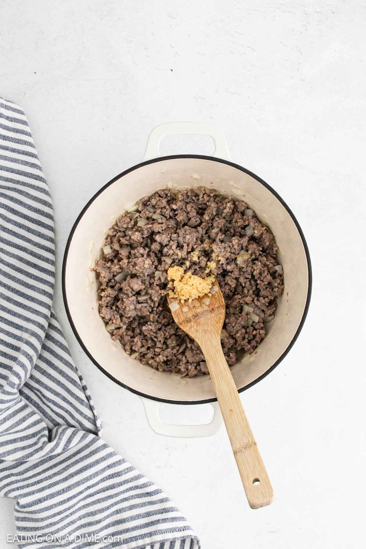 Cooked Italian Sausage in a large pot topped with minced garlic.