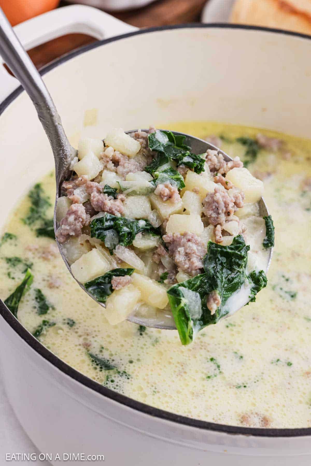 A ladle of soup over the large pot of soup.