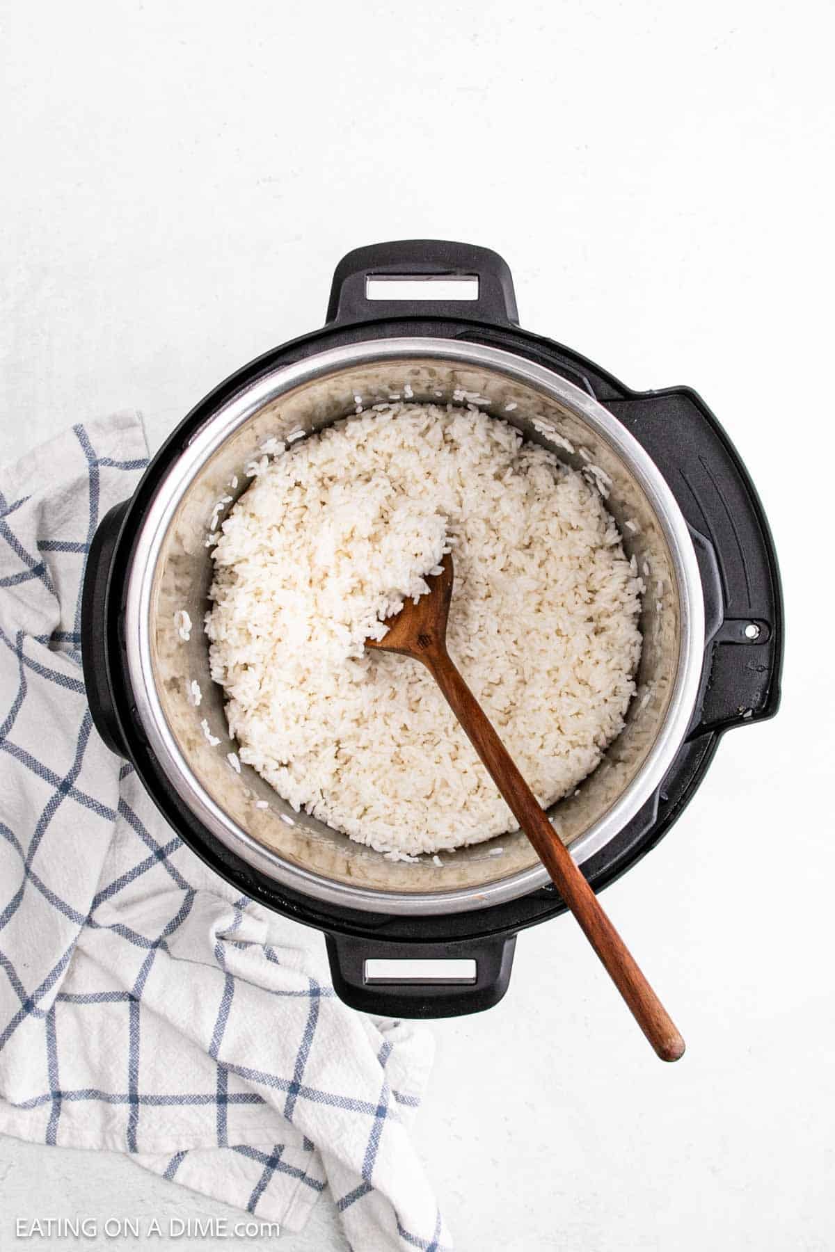Overhead view of fluffy Instant Pot white rice with a wooden spoon, placed on a white surface next to a white and blue checkered kitchen towel.