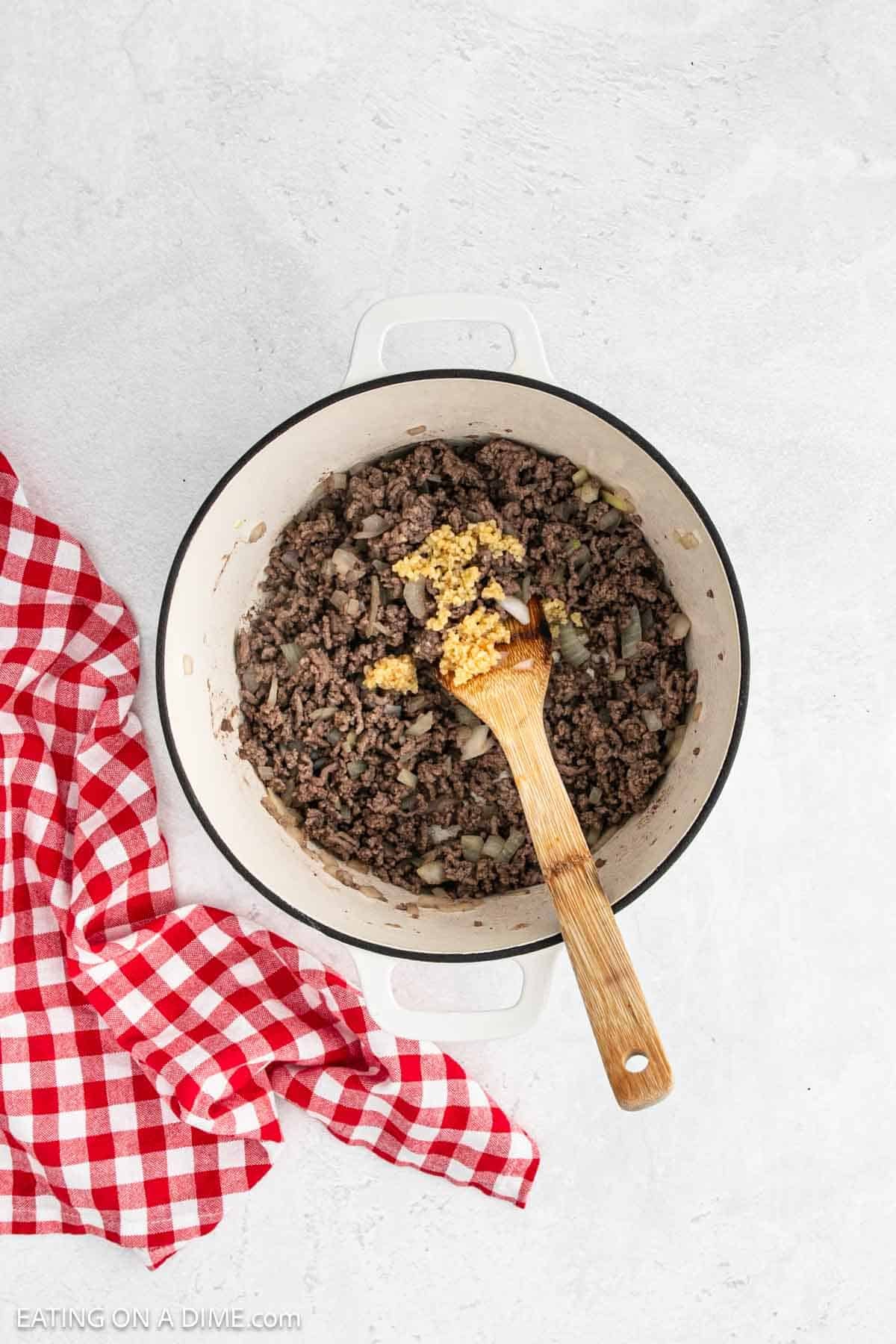 Cooked ground sausage in a large pot topped with minced garlic.