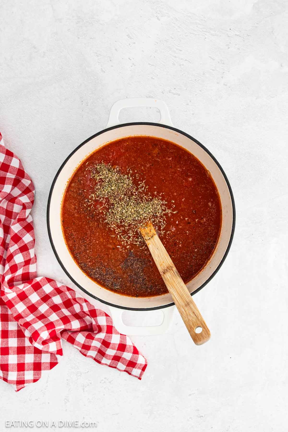Pasta sauce with spices in a large pot with a wooden spoon.