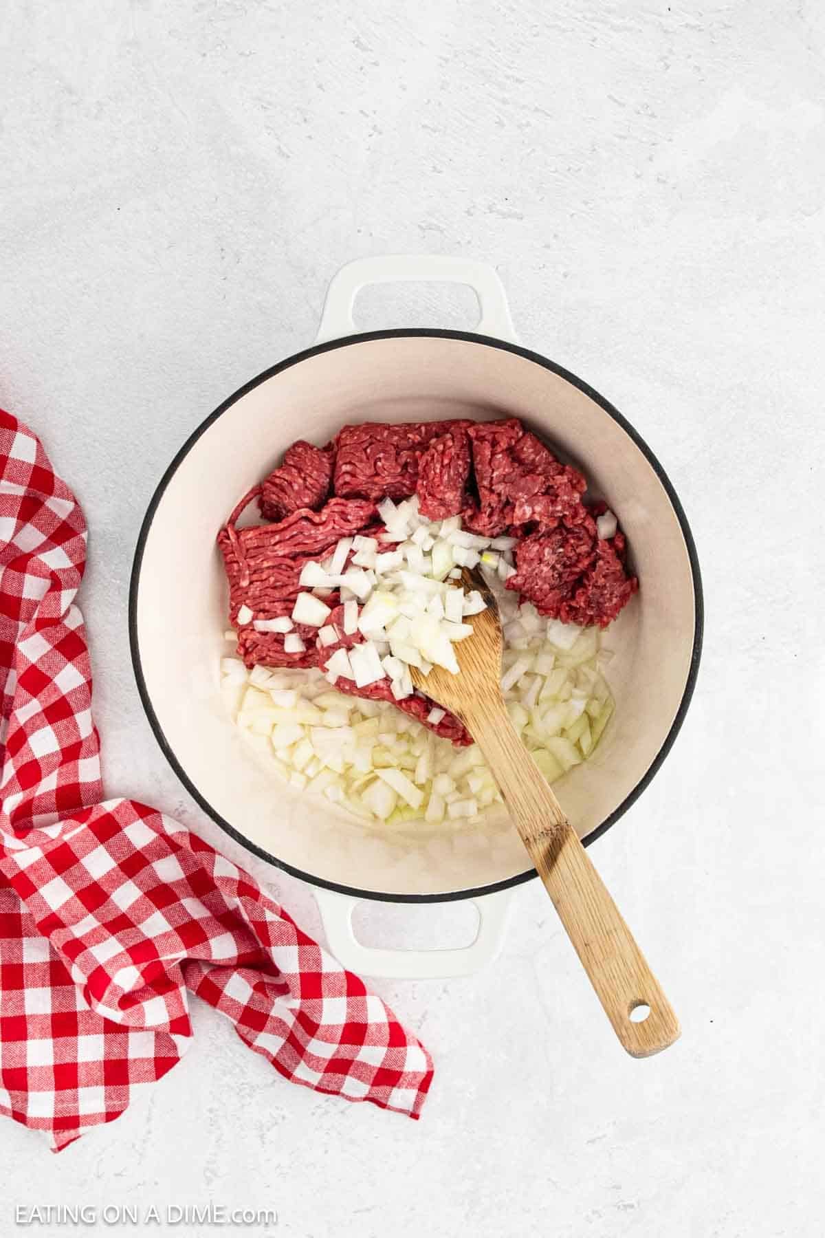 Raw ground beef in a large pot with chopped onions.