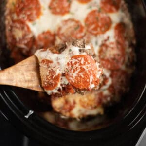 Close up image of pizza casserole in a crock pot with a serving on a wooden spoon.