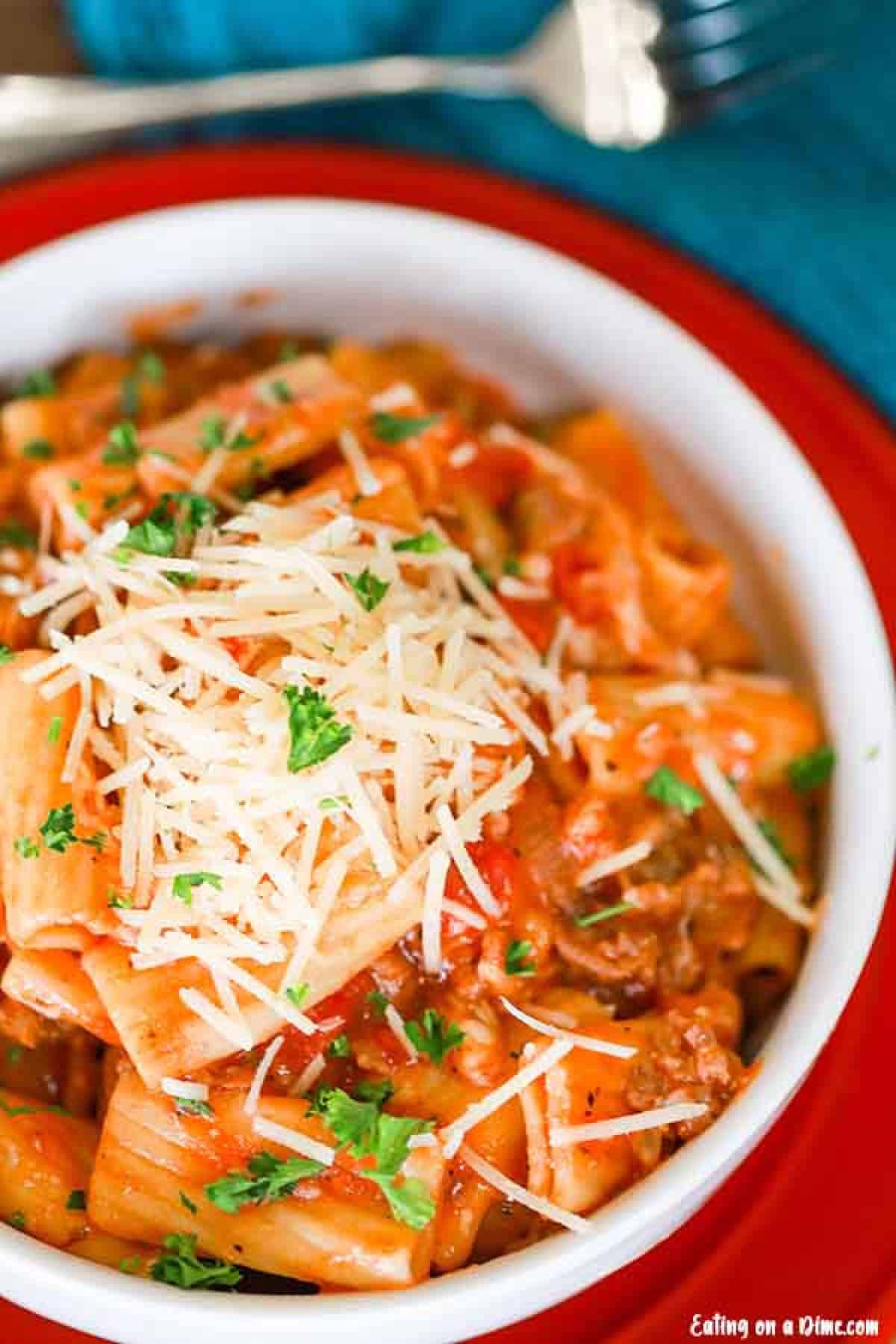 Crock Pot Italian Sausage Rigatoni Recipe is a one pot meal perfect for busy families. The Italian sausage give the pasta amazing flavor for a great meal. Close up image of a white bowl with italian sausage rigatoni on red plate.