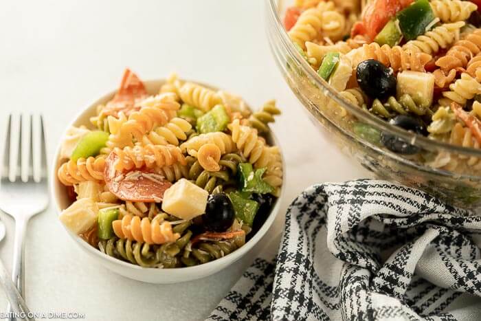 Close up image of Italian Pasta Salad in a clear bowl with a small serving on the side with a fork. 