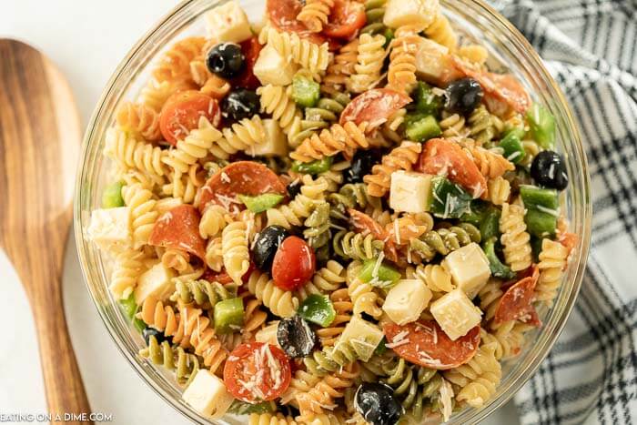 Close up image of Italian Pasta Salad in a clear bowl with a wooden spoon. 