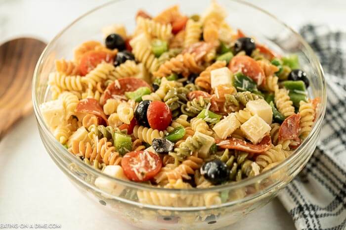 Close up image of Italian Pasta Salad in a clear bowl with a wooden spoon. 