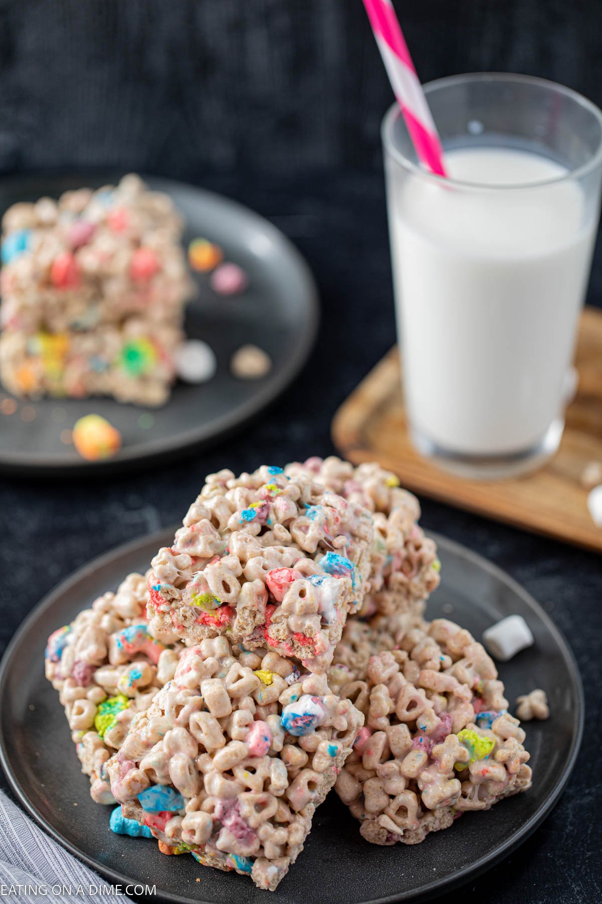 A stack of lucky charm treats on a charcoal plate with a glass of milk behind them.  