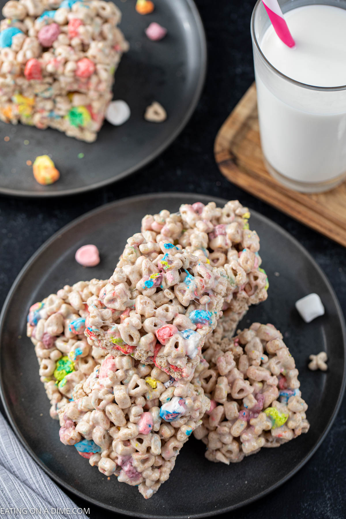 A stack of lucky charm treats on a charcoal plate with a glass of milk behind them.  