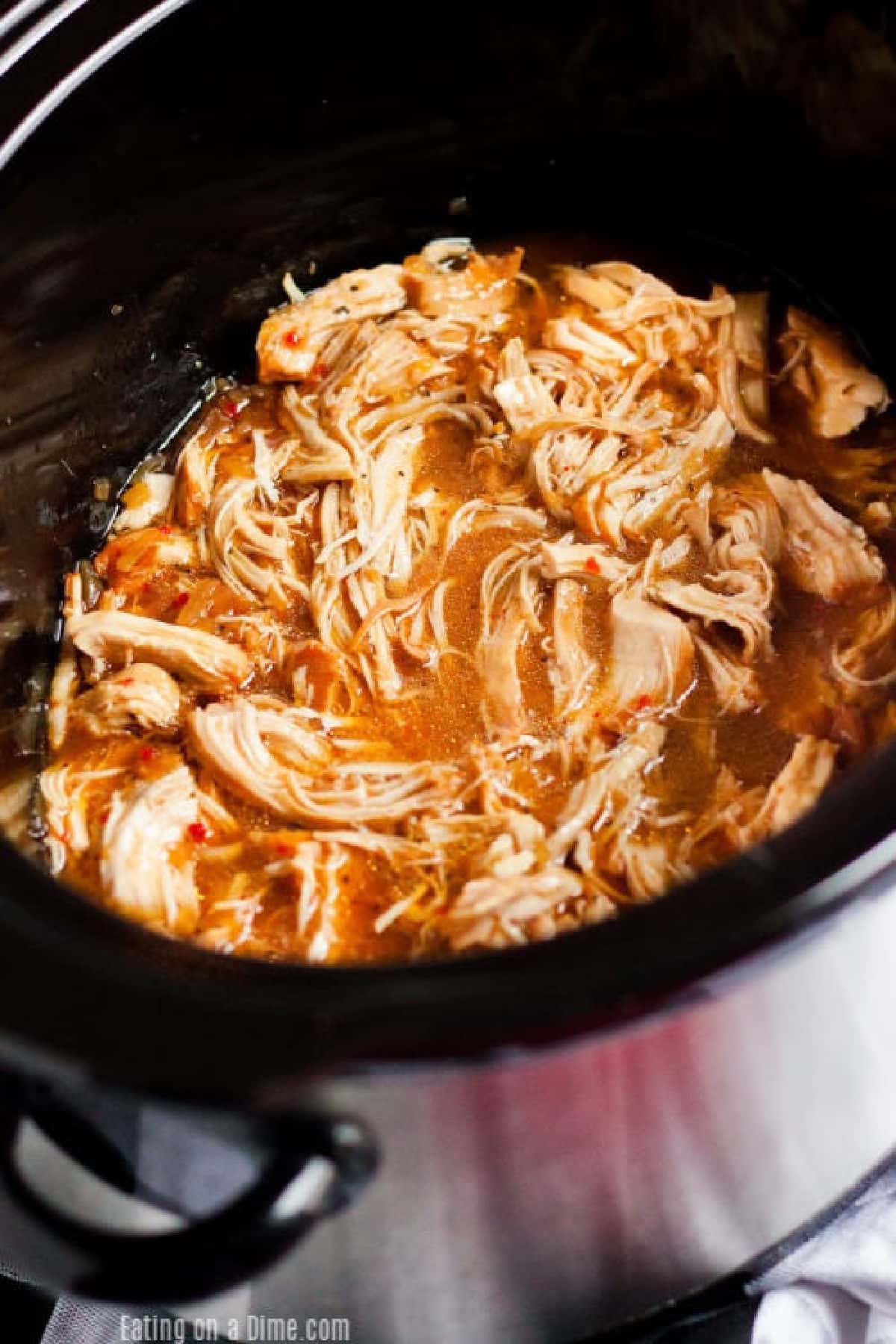 Crockpot Savory Chicken simmers in a flavorful broth inside a black slow cooker. The tender, shredded chicken soaks up the sauce, with visible seasonings throughout this comforting dish.