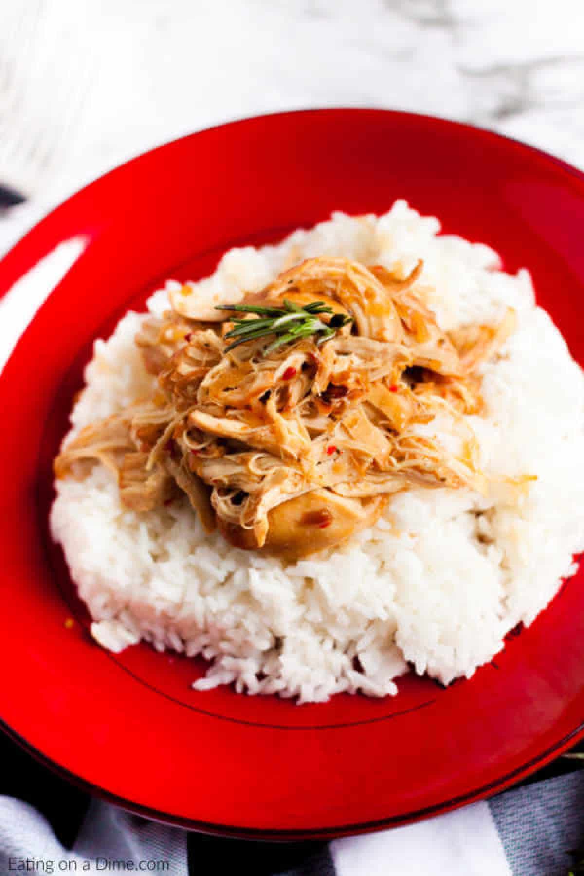 Crock pot savory chicken recipe is one of those easy recipes that sounds too good to be true but taste amazing. With just 3 ingredients, dinner is a breeze. A red plate filled with white rice, topped with Crockpot Savory Chicken and garnished with a small sprig of rosemary.