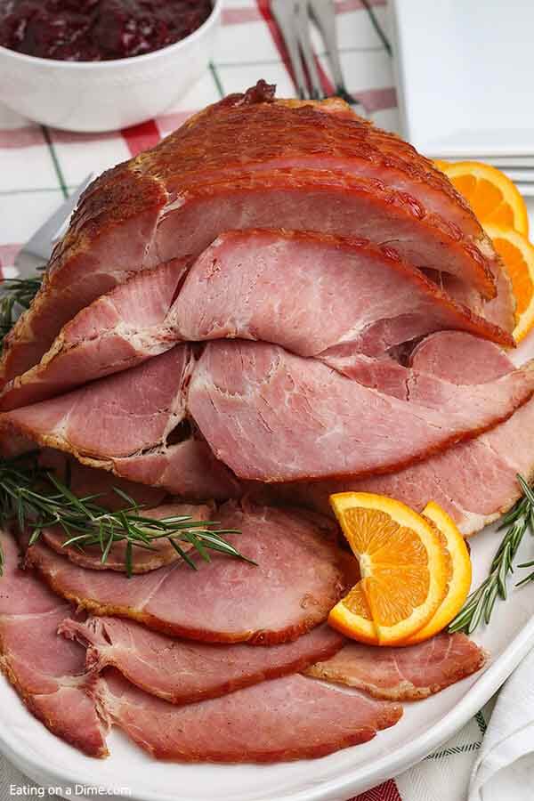 Close up image of sliced spiral ham on a platter with slice oranges and herbs. 
