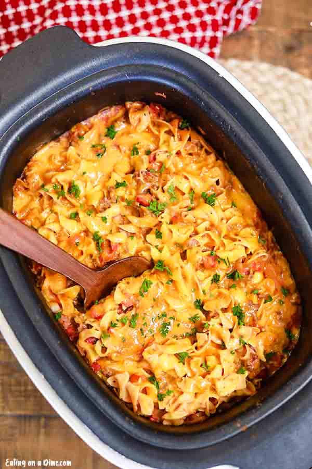 Close up image of beef and noodle casserole in the crock pot with a wooden spoon. 