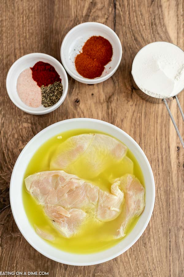 Close up image of chicken being marinated in pickle juice and seasoning on the side. 