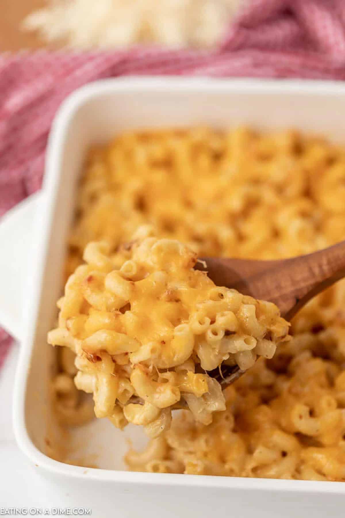 Close up image of mac and cheese in a baking dish with a serving on a wooden spoon. 