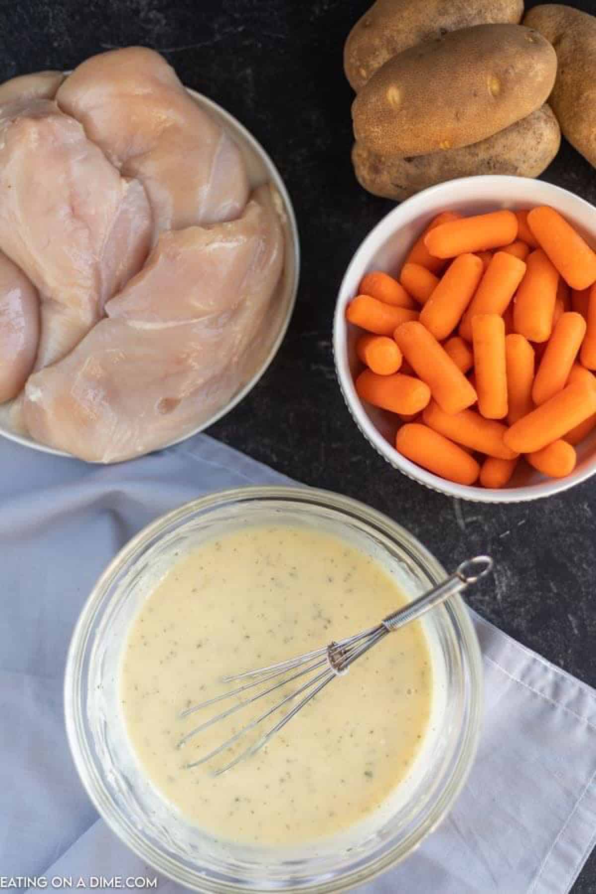 Combining the sauce ingredients in a bowl with a whisk with a plate of chicken breast, bowl of carrots and Russet Potatoes