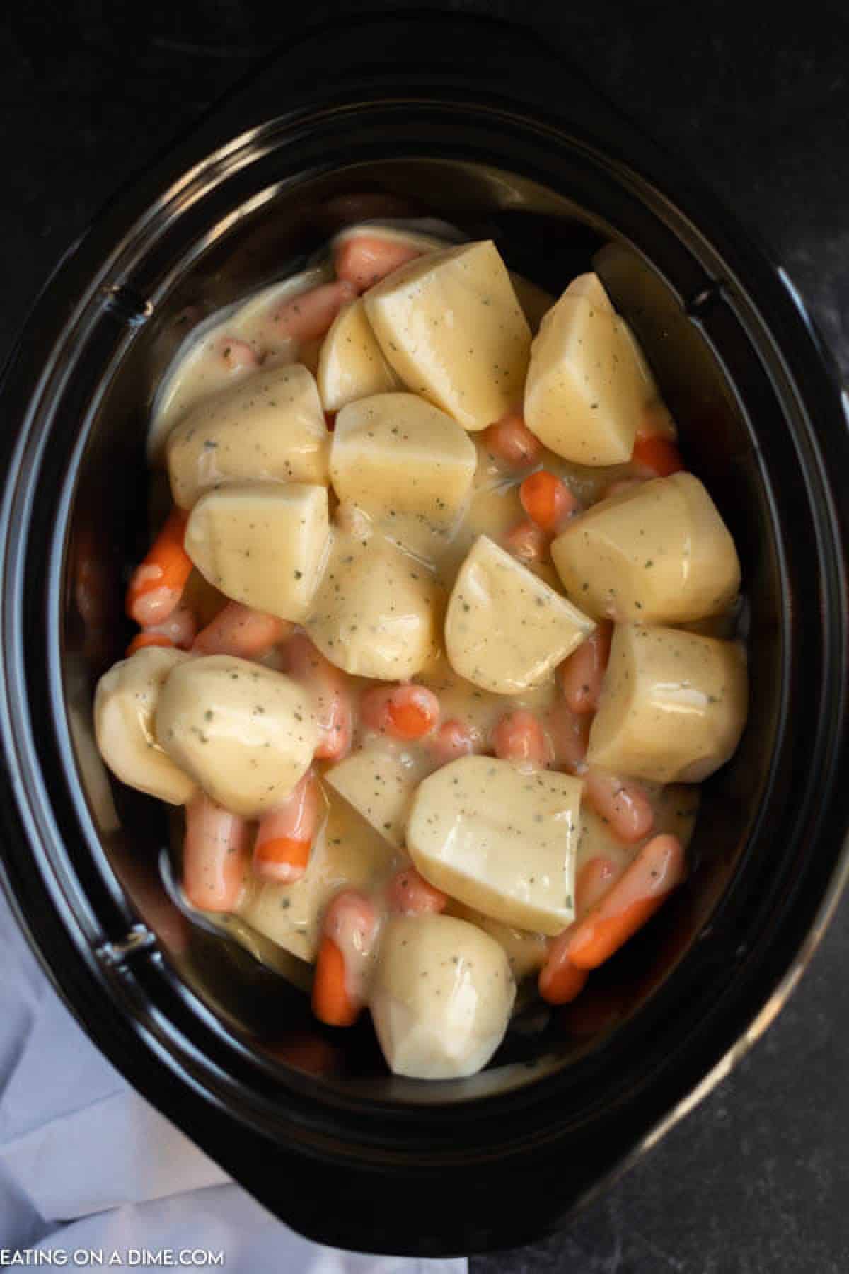 Diced potatoes, baby carrots in a creamy sauce in the slow cooker