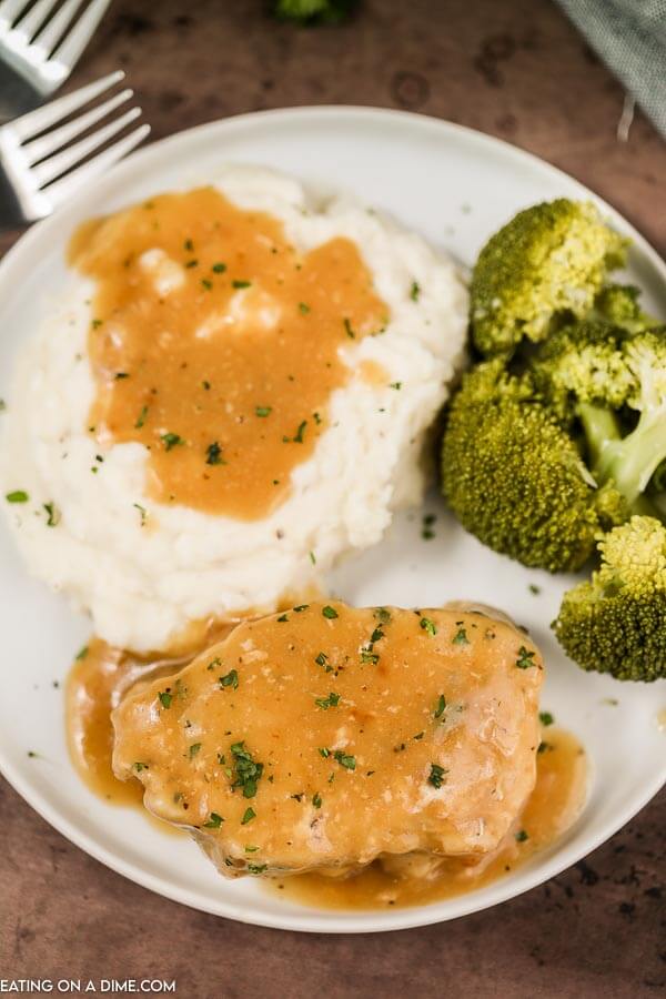 Close up image of pork chops and gravy with a side of mashed potatoes and broccoli on a white plate. 