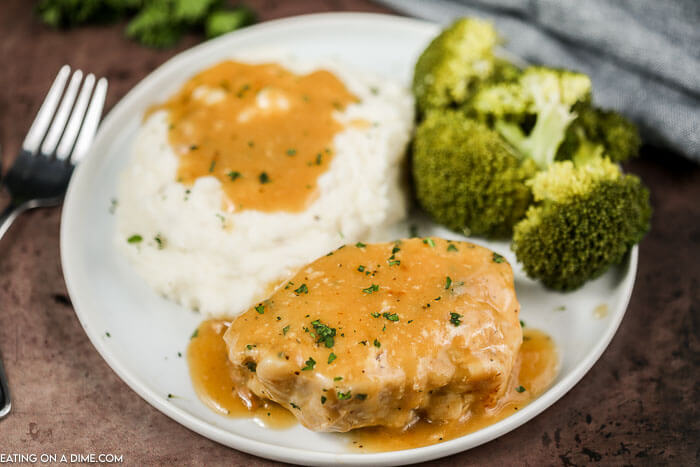 Close up image of pork chops and gravy with a side of mashed potatoes and broccoli on a white plate. 