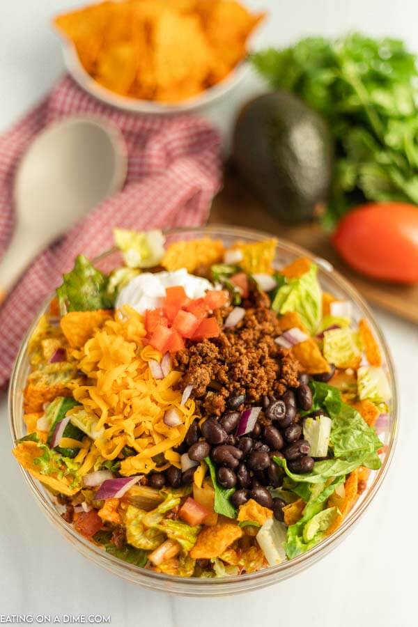 a bowl of taco salad topped with sour cream and diced avocado, cheese, and black beans
