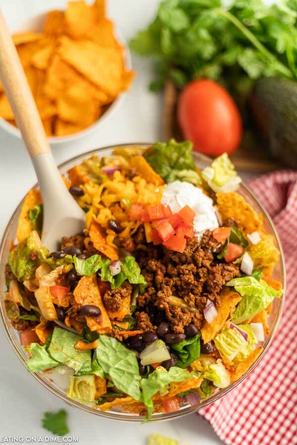 a bowl of taco salad topped with sour cream and diced avocado with a spoon