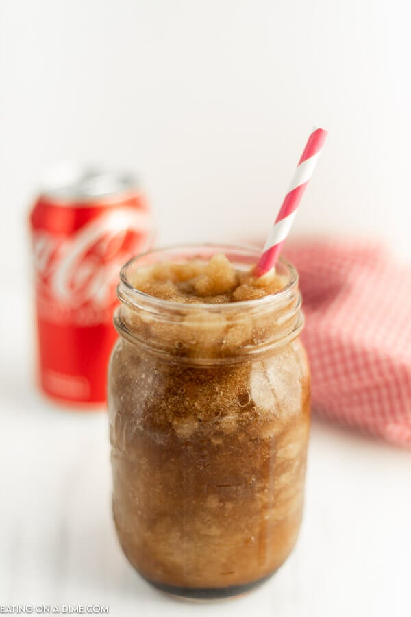 Close up image of a coke slushie in a mason jar with a straw and a can of coca-cola. 