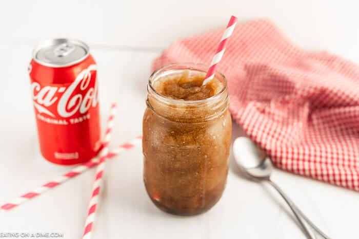 Close up image of a coke slushie in a mason jar with a straw and a can of coca-cola. 