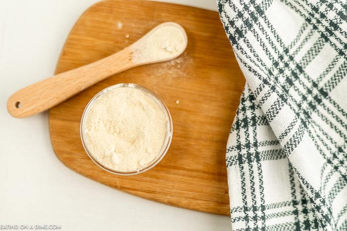 Close up image of garlic powder in a jar with a teaspoon on a cutting board. 