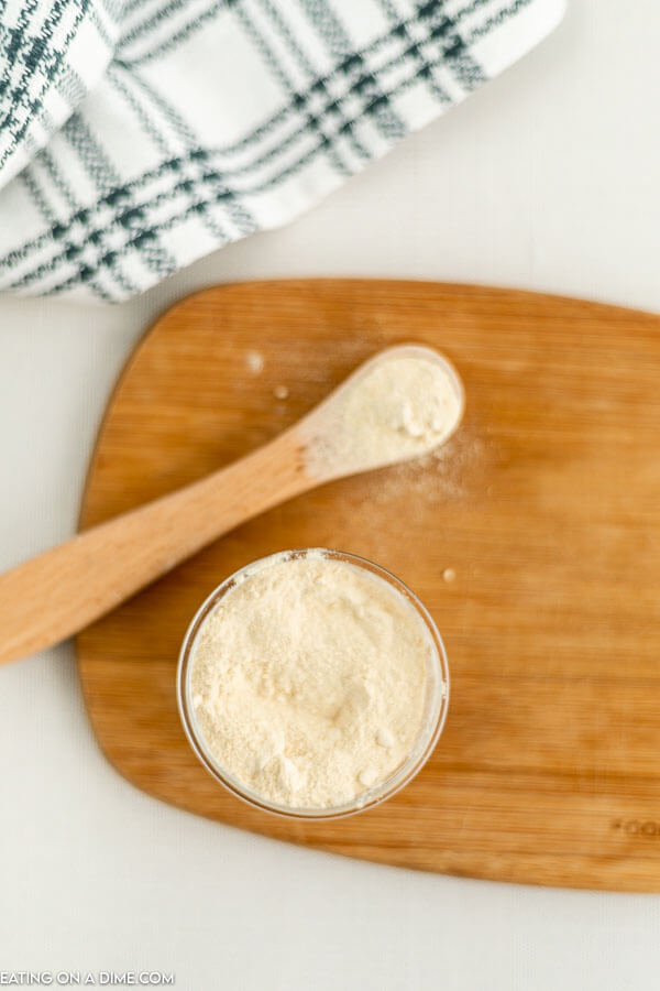 Close up image of garlic powder in a jar with a teaspoon on a cutting board. 