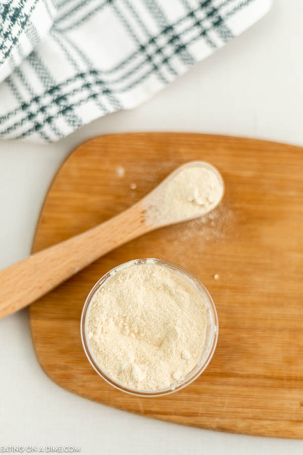 Close up image of garlic powder in a jar with a teaspoon on a cutting board. 