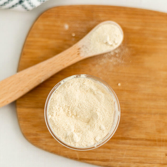 Close up image of garlic powder in a jar with a teaspoon on a cutting board. 