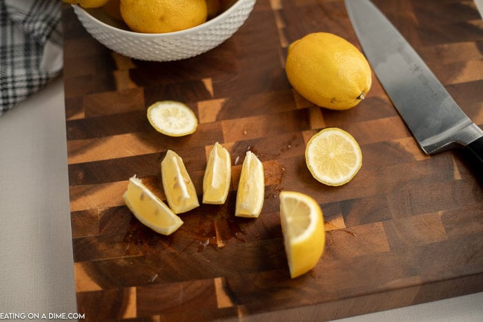 Close up image of a bowl of lemons with a lemon wedges on the cutting board. 